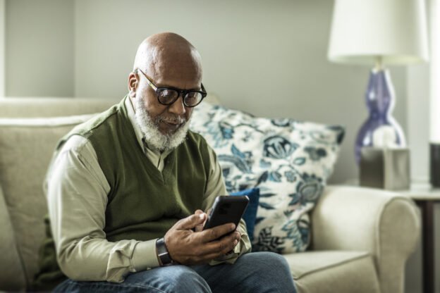 Older gentleman sitting on couch looking at smartphone